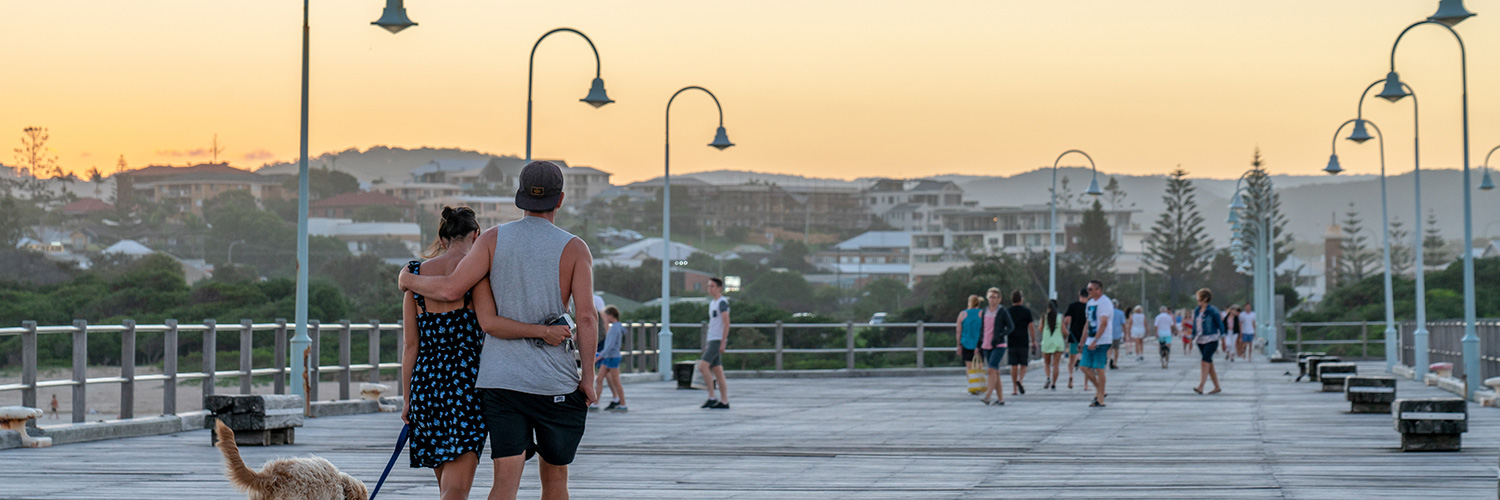 Couple walking their dog along Coffs Harbour jetty boardwalk.