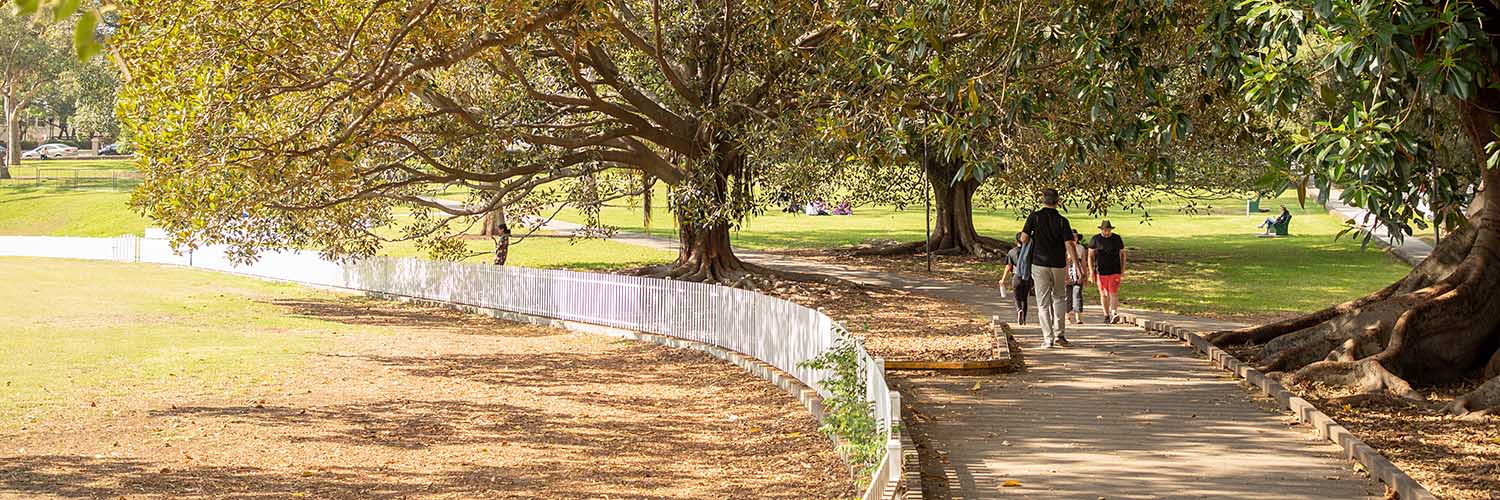 People walking on pathway besides a cricket oval.