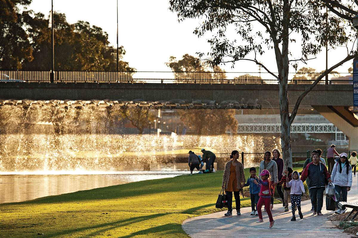 A family walking alongside Parramatta River with overhead bridge in background. Credit: Don Fuchs