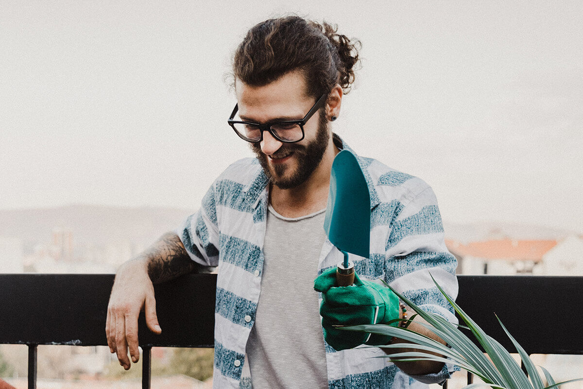 Person looking happy and holding a spade. There are potted plants in front of them.